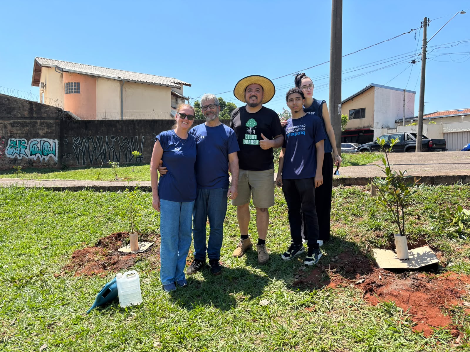 Equipe Marsh e participante do Fruto Urbano na praça, ao lado de mudas com papelão e protetores de PVC.