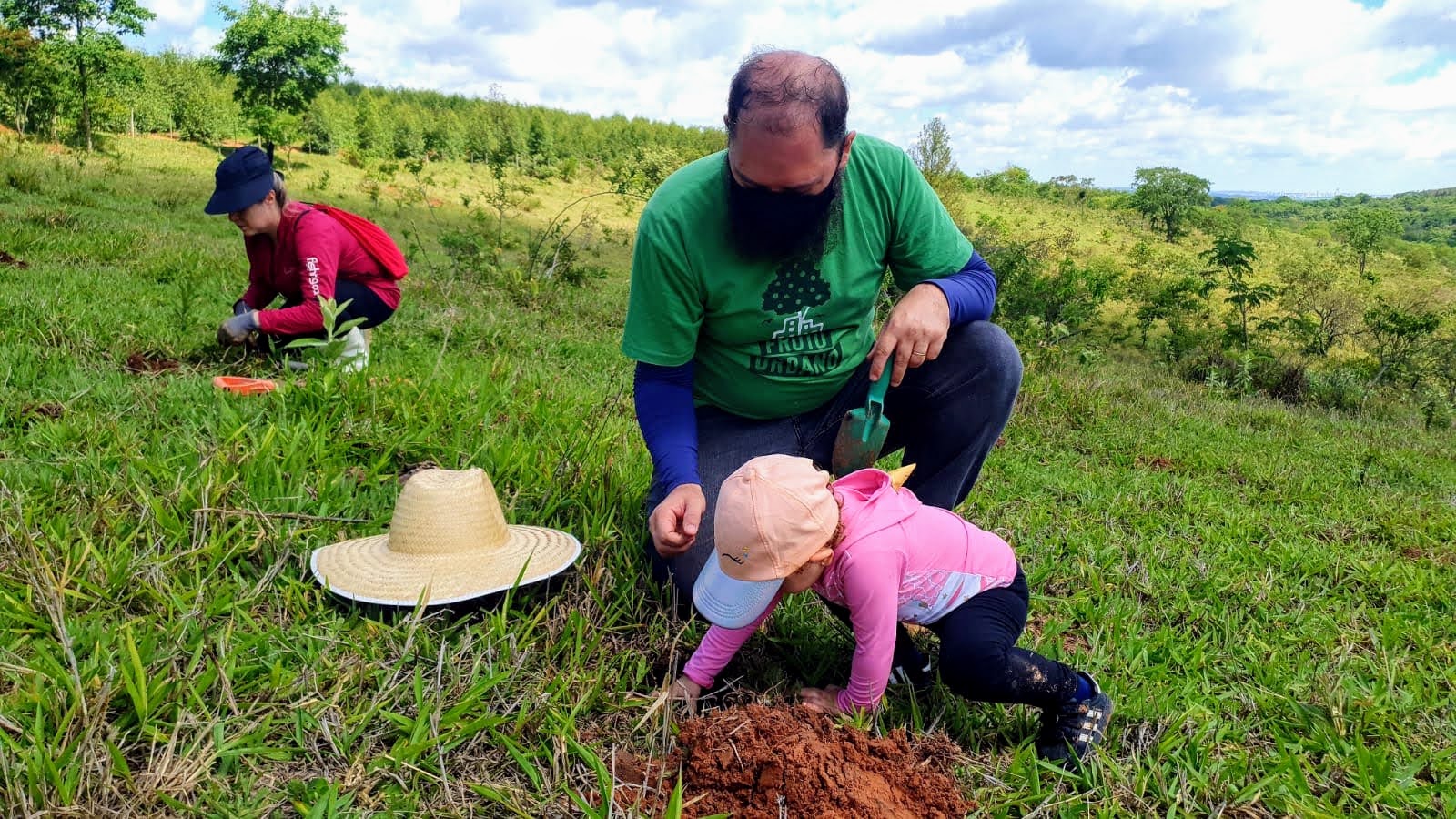 Adulto e criança participando do plantio de uma muda